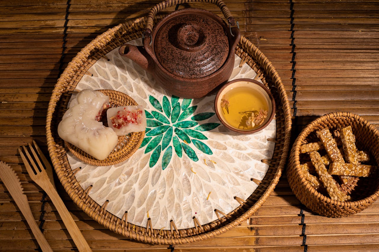 Top view of a traditional Asian tea set with pastries and snacks on a bamboo mat, highlighting cultural cuisine.