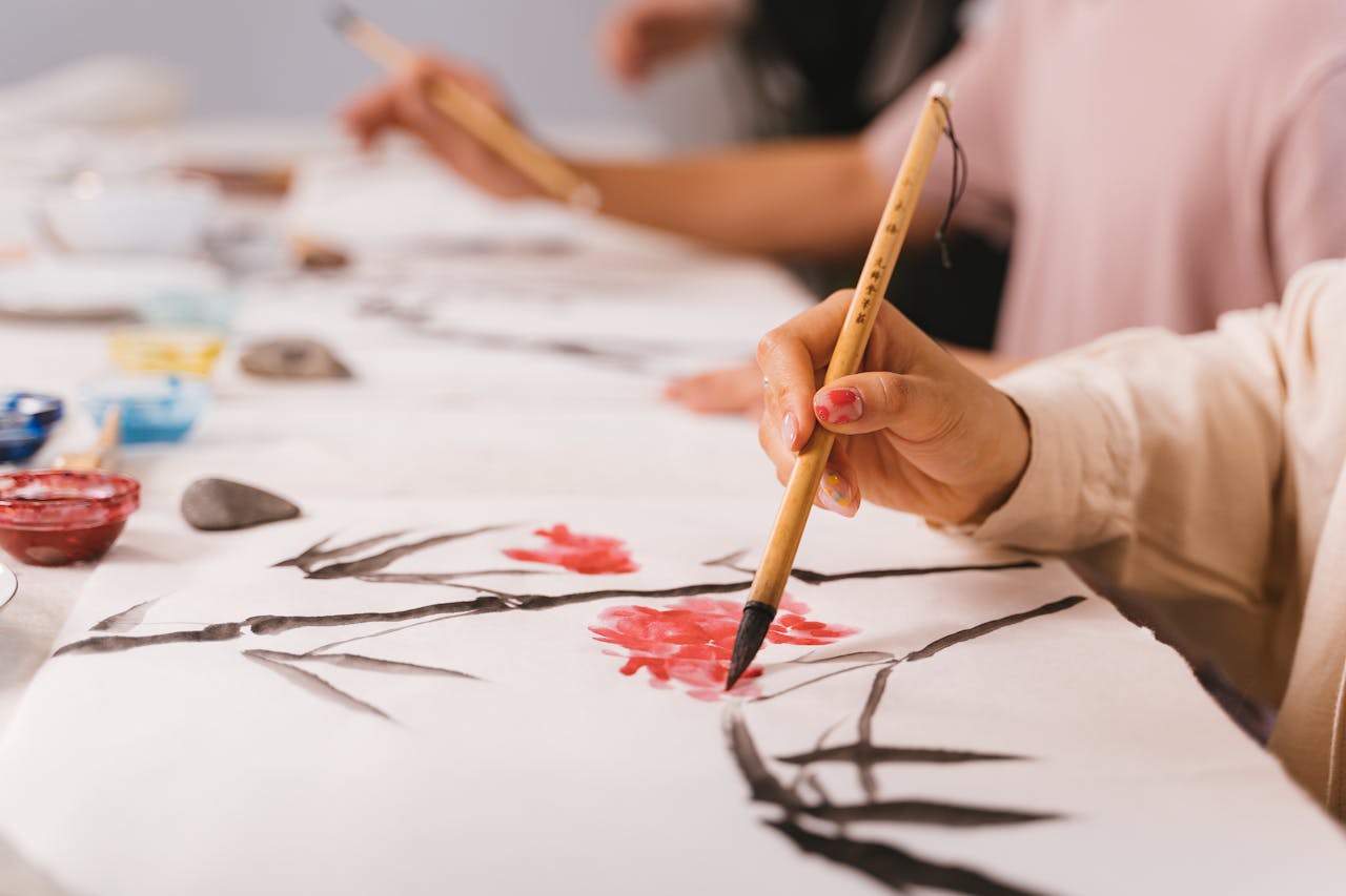 Detailed shot of hands practicing traditional Asian brush painting with vibrant colors, indoors.